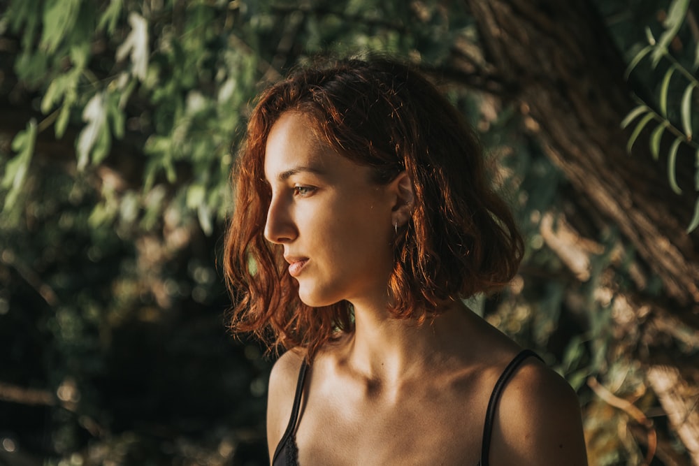 Une femme aux cheveux roux debout devant un arbre