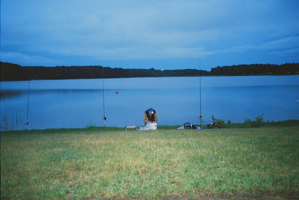 a woman sitting on a grass covered field next to a lake