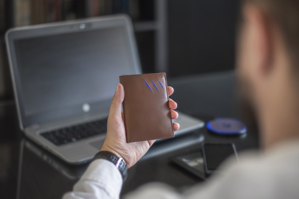 a man holding a notebook in front of a laptop