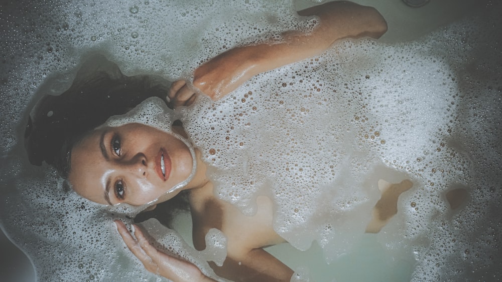 a woman laying in a bathtub with foam on her face