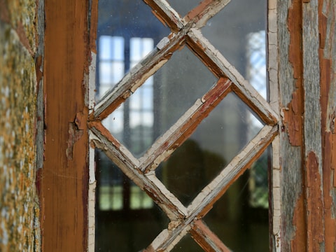 A close-up of worn-out wooden windows with peeling paint and visible drafts.