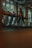 A person is walking on a treadmill in a dimly lit gym with large windows providing natural light. The individual is dressed in athletic wear and the indoor plants outside the windows add a touch of nature to the modern gym environment.