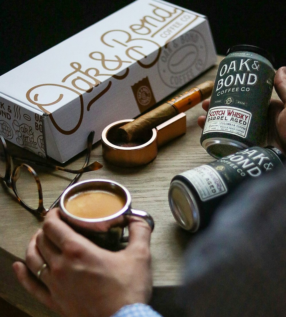 a man holding a cup of coffee next to a box of coffee