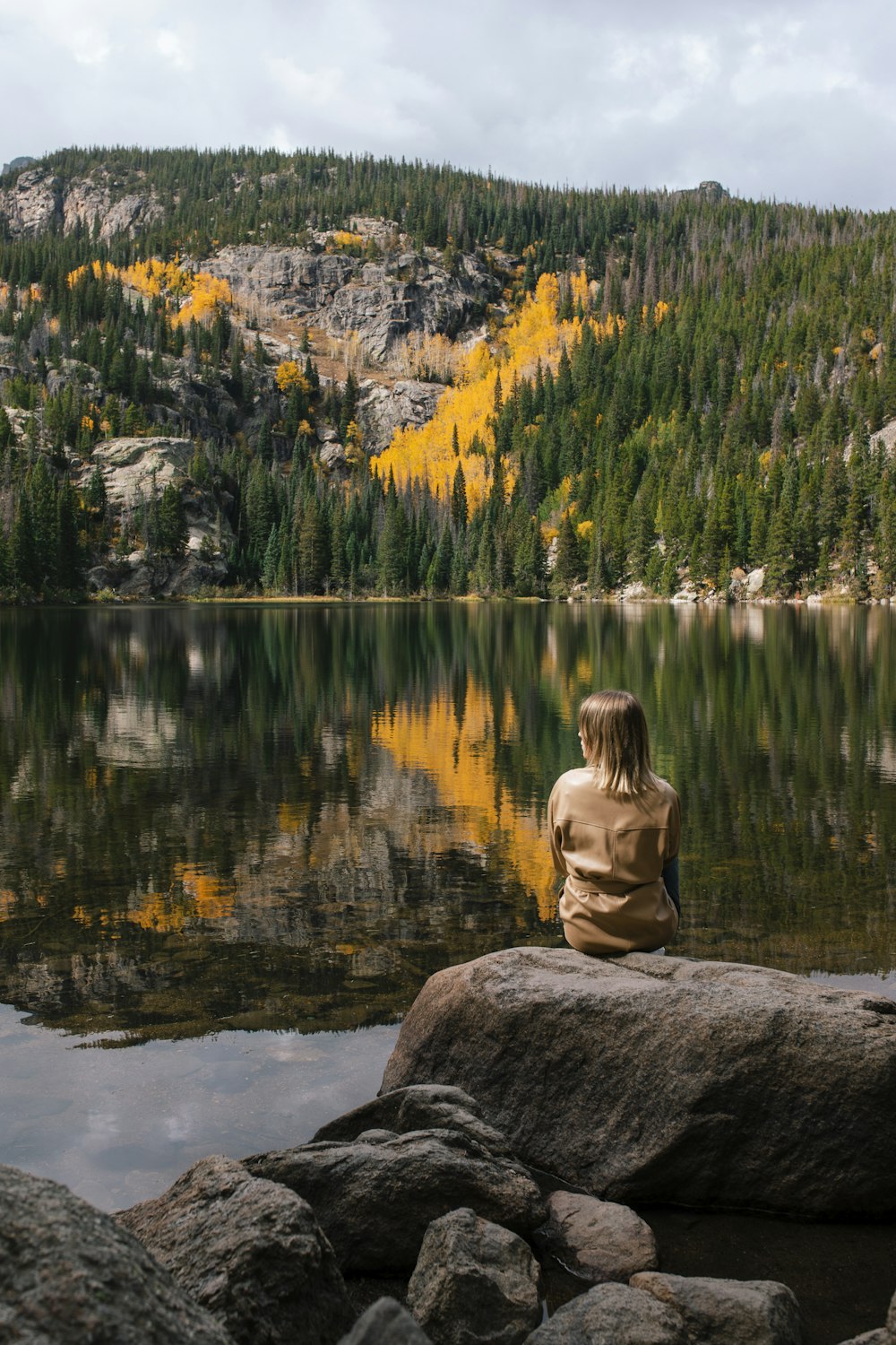 a person sitting on top of a rock near a lake