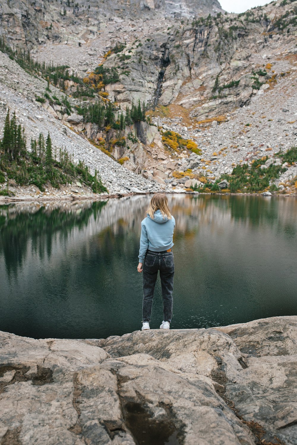 Una mujer parada en la cima de una roca junto a un lago
