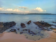 A peaceful coastal scene with gentle waves lapping against weathered rocks under a cloudy sky.