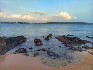 A peaceful coastal scene with gentle waves lapping against weathered rocks under a cloudy sky.
