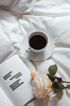 A serene morning scene with a steaming cup of coffee on a cozy blanket, surrounded by soft purple flowers.