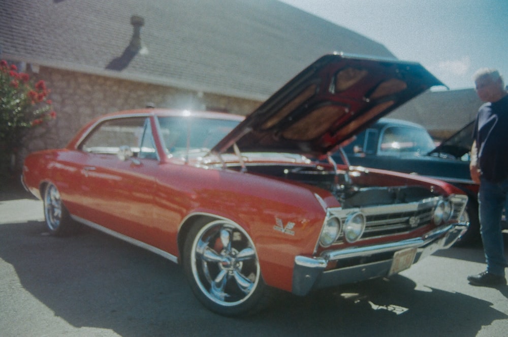 a man standing next to a red car with its hood open