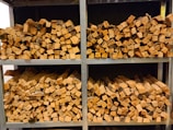 Several stacks of neatly chopped firewood are arranged on metal shelves. The wood pieces have a natural, rustic appearance with varying shades of brown and some visible bark. The shelves are organized in a neat and orderly fashion.