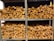 Several stacks of neatly chopped firewood are arranged on metal shelves. The wood pieces have a natural, rustic appearance with varying shades of brown and some visible bark. The shelves are organized in a neat and orderly fashion.