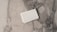 A stack of white business cards is placed on a grey and white marble surface. The surface displays a natural pattern with a mix of light and dark grey tones, creating a sleek and polished look.