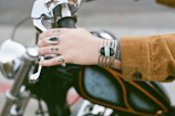 Hand wearing a thick leather biker bracelet resting on a motorcycle handlebar.