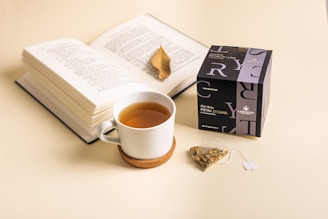 A steaming cup of herbal tea resting beside an open recipe journal on a warm taupe table