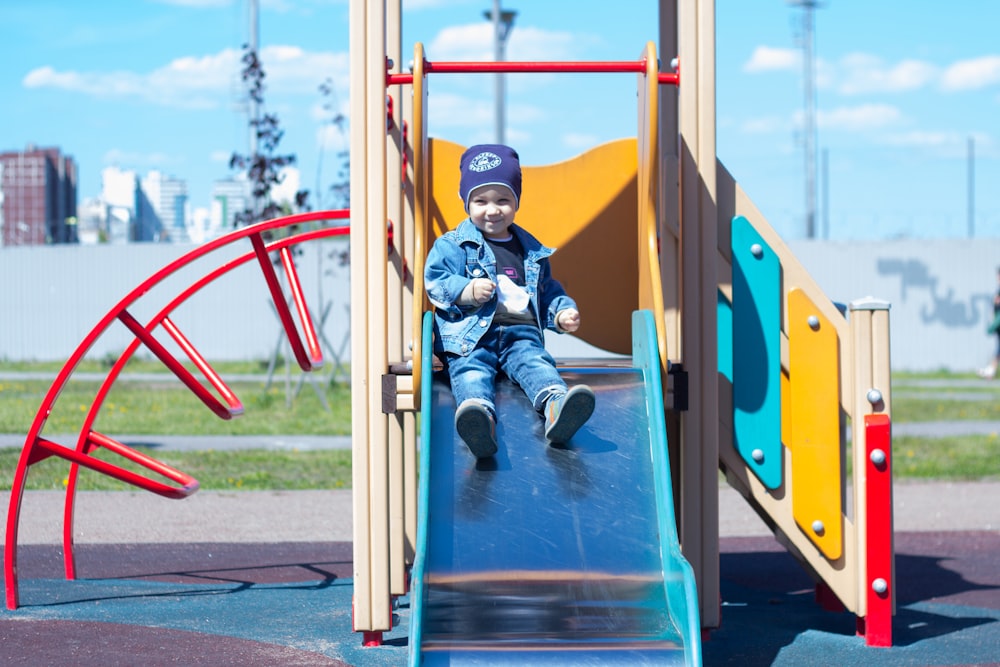 a little boy sitting on a slide at a playground