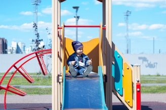 a little boy sitting on a slide at a playground