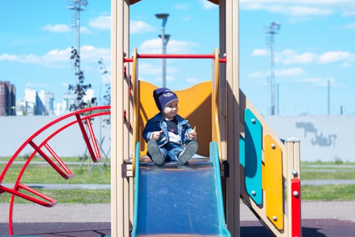 a little boy sitting on a slide at a playground