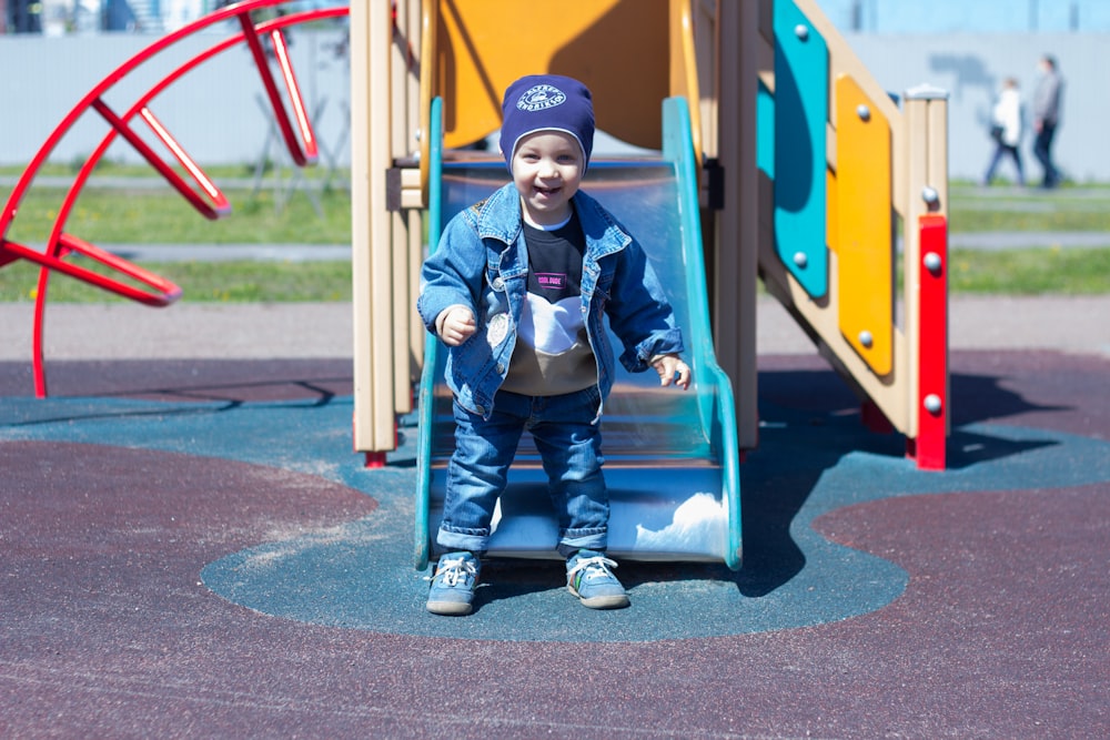 a little boy standing on a slide at a playground