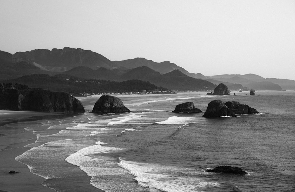 a black and white photo of a beach with mountains in the background
