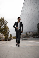Man dressed in a sleek black suit standing confidently by modern architecture