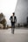 A stylishly dressed man walking confidently in a modern urban setting.