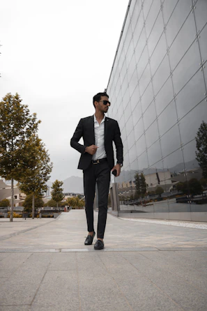Man dressed in a sleek black suit standing confidently by modern architecture