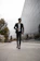 A stylish man confidently walking in a sleek black tracksuit against a cityscape backdrop.