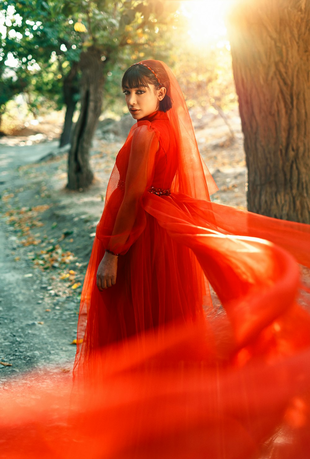 a woman in a red dress is standing in the woods