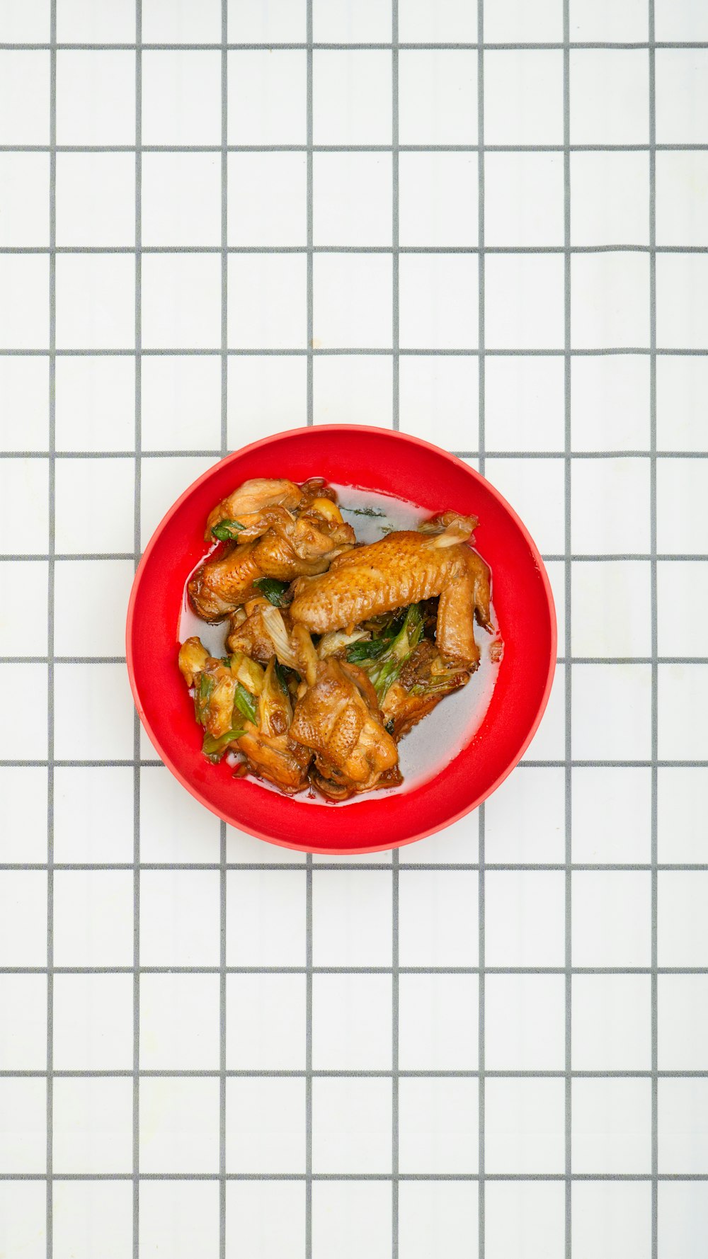 a red plate filled with chicken wings on top of a white tiled floor