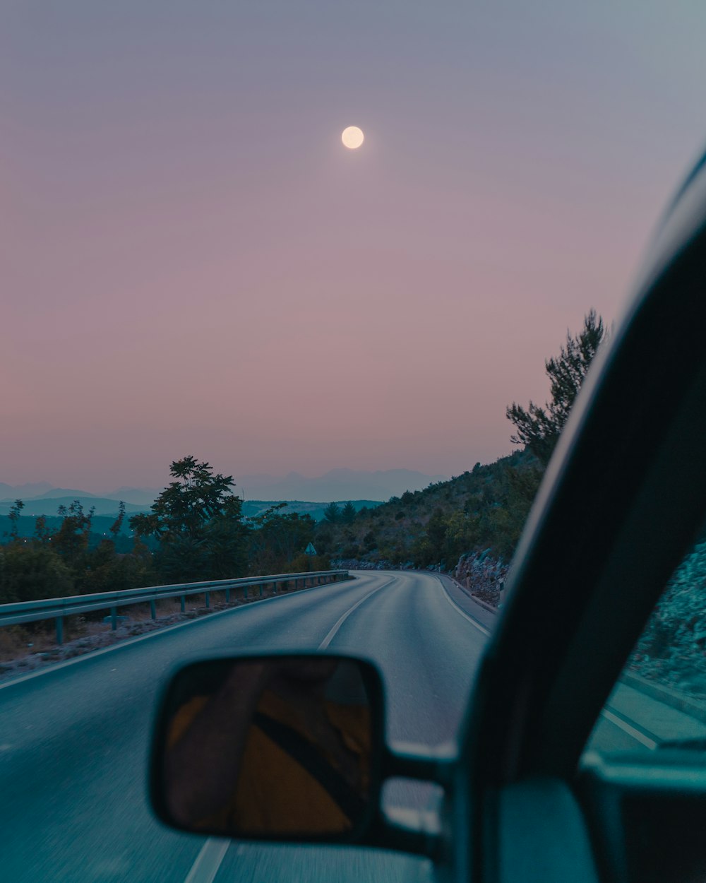 a car driving down a road with the moon in the sky