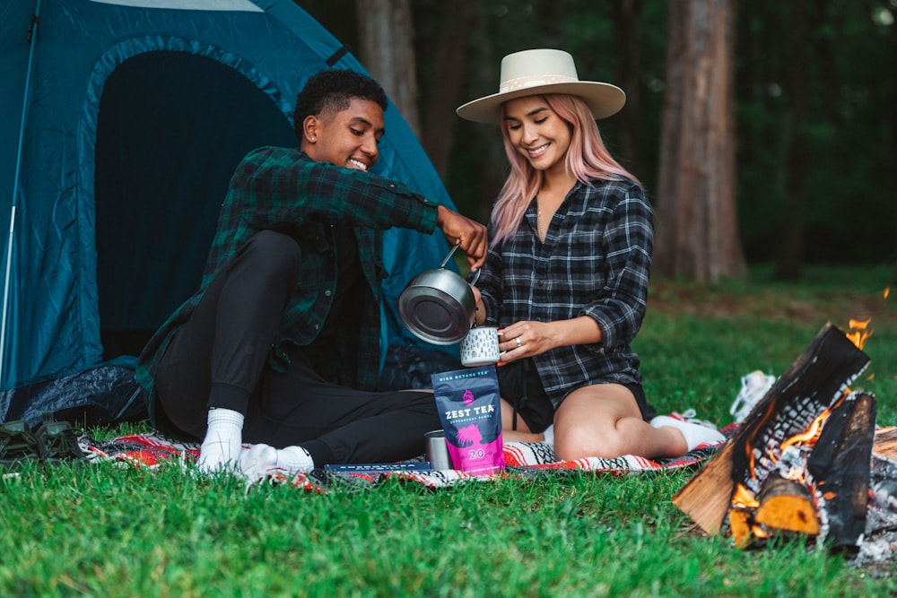 a man and woman sitting on a blanket next to a tent