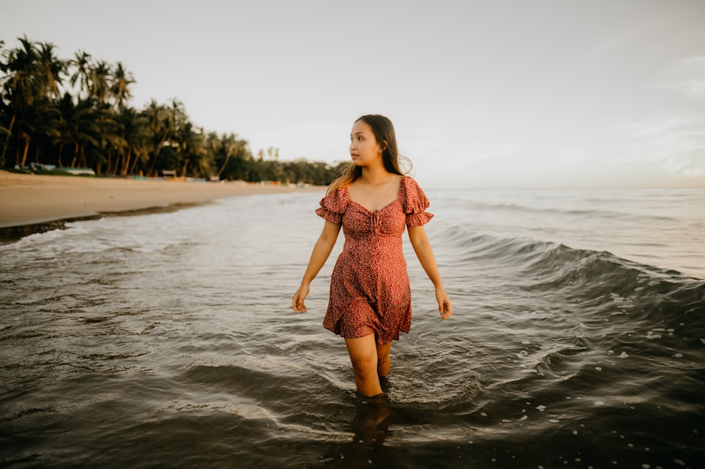 a woman in a red dress walking into the ocean