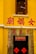 A yellow building with a window featuring metal bars above a doorway. Red Chinese characters are prominently displayed on the walls and above the door. The entrance is adorned with traditional red banners featuring calligraphy.