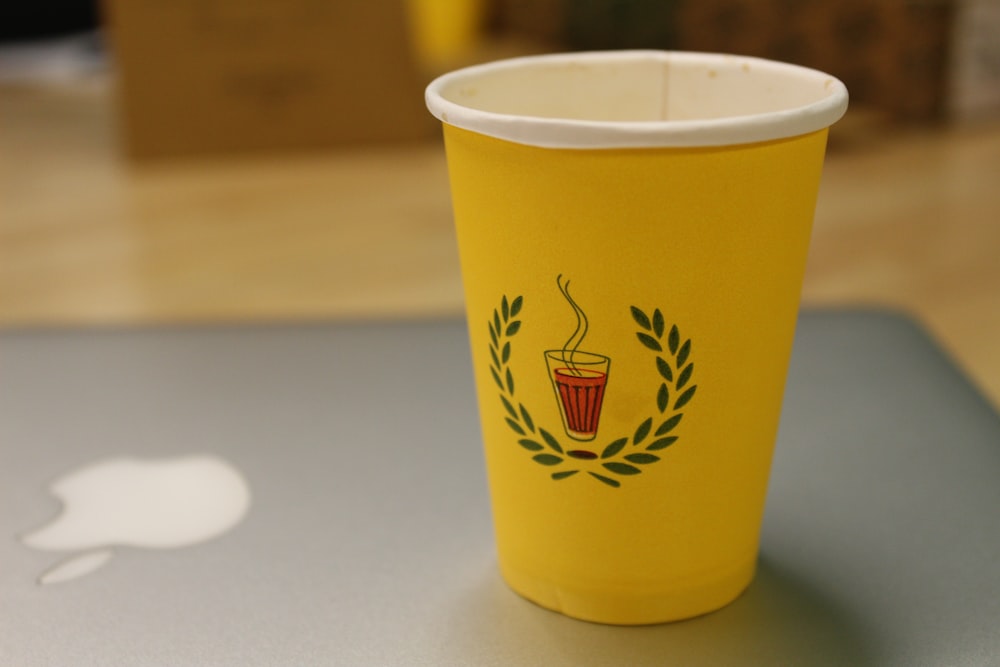 a yellow cup sitting on top of a laptop computer