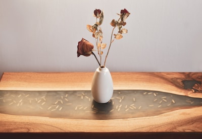 Close-up of elegant ceramic vase with dried flowers on a wooden table.