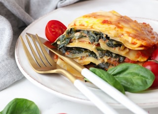 a white plate topped with lasagna covered in spinach