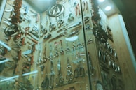 A display cabinet filled with a variety of scissors and cutting tools. The tools are arranged neatly against a wooden backdrop and include different types of scissors, knives, and multi-tools. The scene is decorated with Christmas-themed ornaments, such as tinsel and metallic decorations hanging from above.