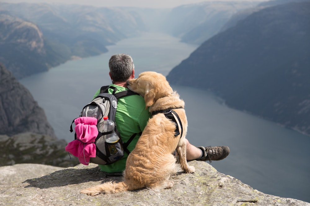 Un uomo seduto su una roccia con un cane sulla schiena