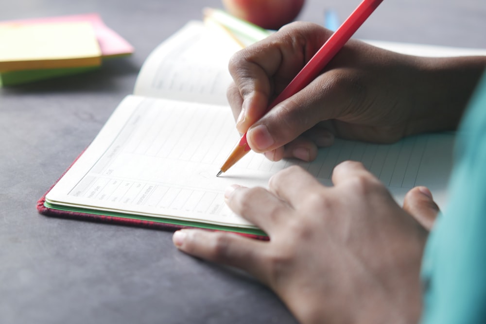 a person writing on a notebook with a pencil