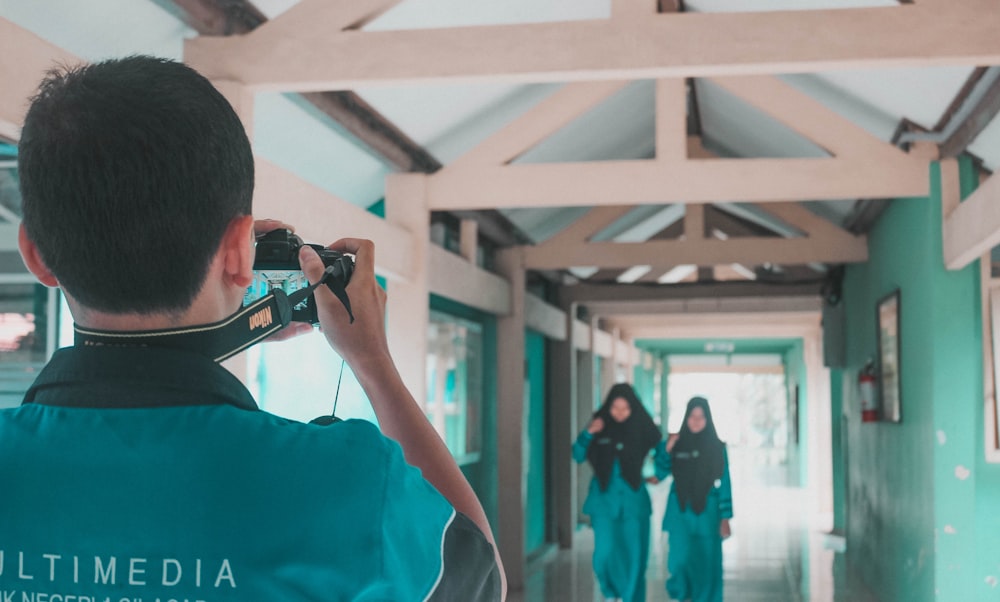 a man taking a picture of a woman walking down a hallway