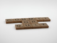 Wooden Scrabble tiles are arranged to display the words 'COMMIT OR QUIT' on a plain white background.