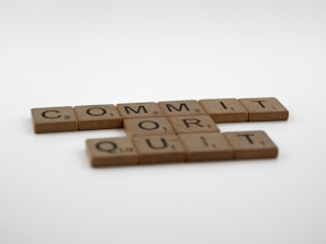 Wooden Scrabble tiles are arranged to display the words 'COMMIT OR QUIT' on a plain white background.