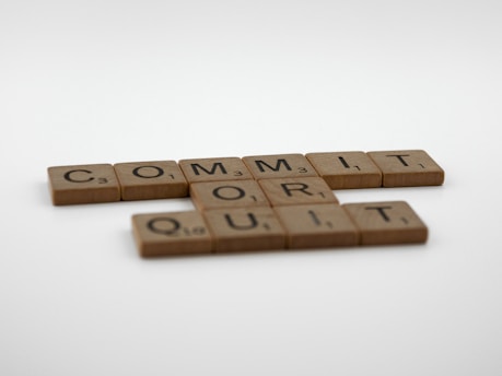 Wooden Scrabble tiles are arranged to display the words 'COMMIT OR QUIT' on a plain white background.