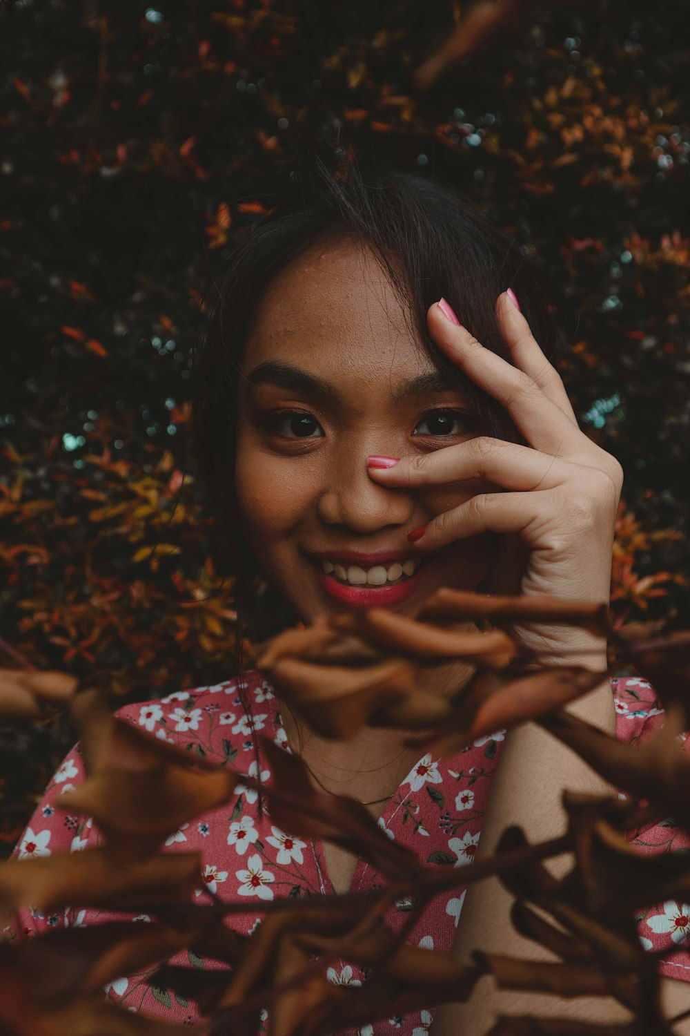 a woman with a pink flowered shirt holding her hand up to her face