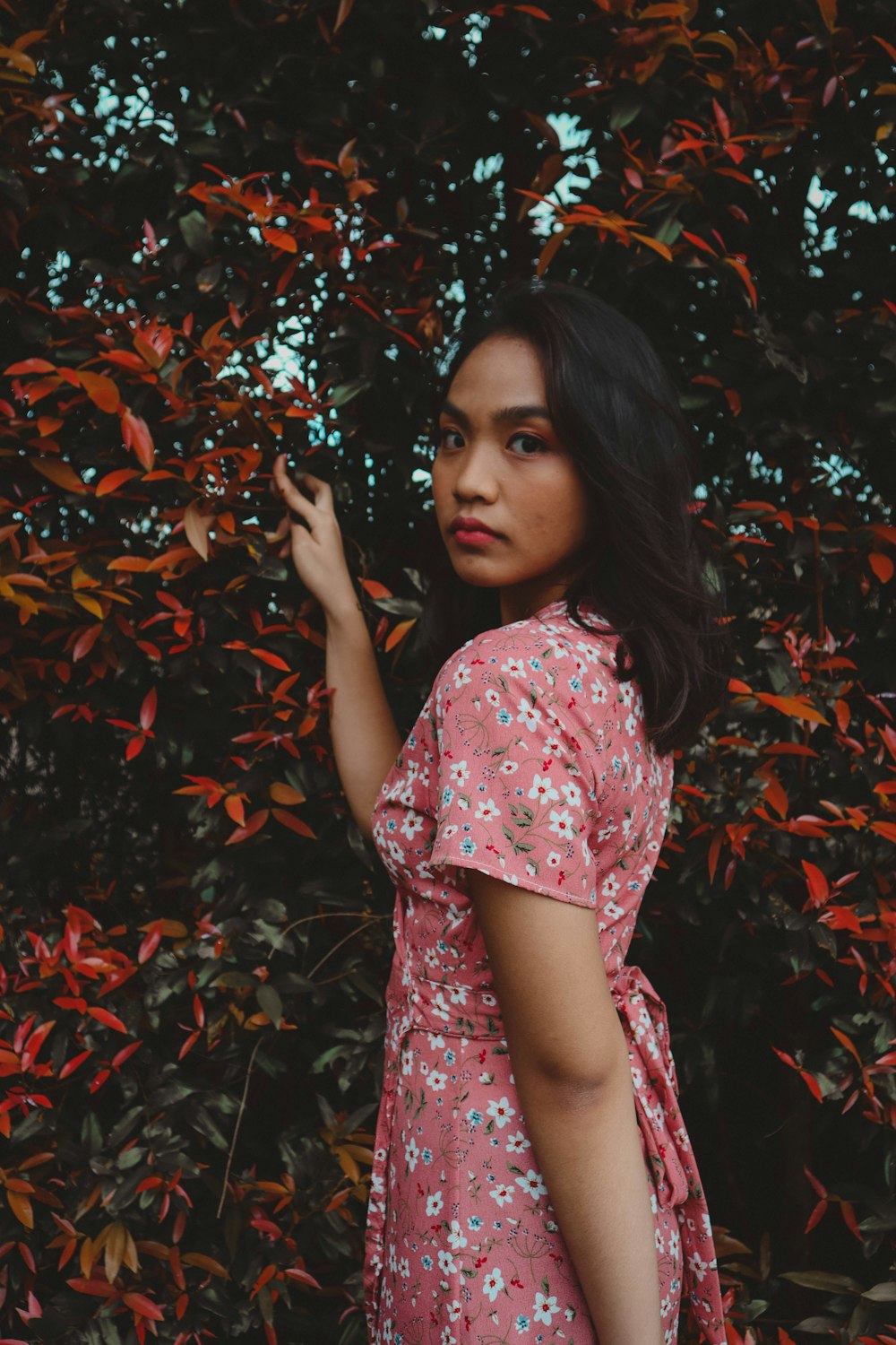 a woman in a pink dress standing in front of a bush