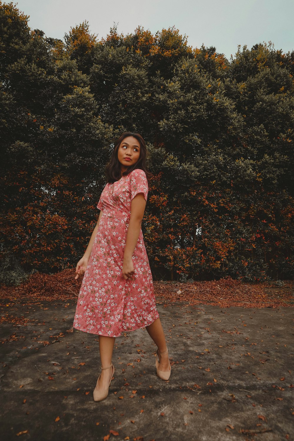 a woman in a pink dress standing in front of some trees