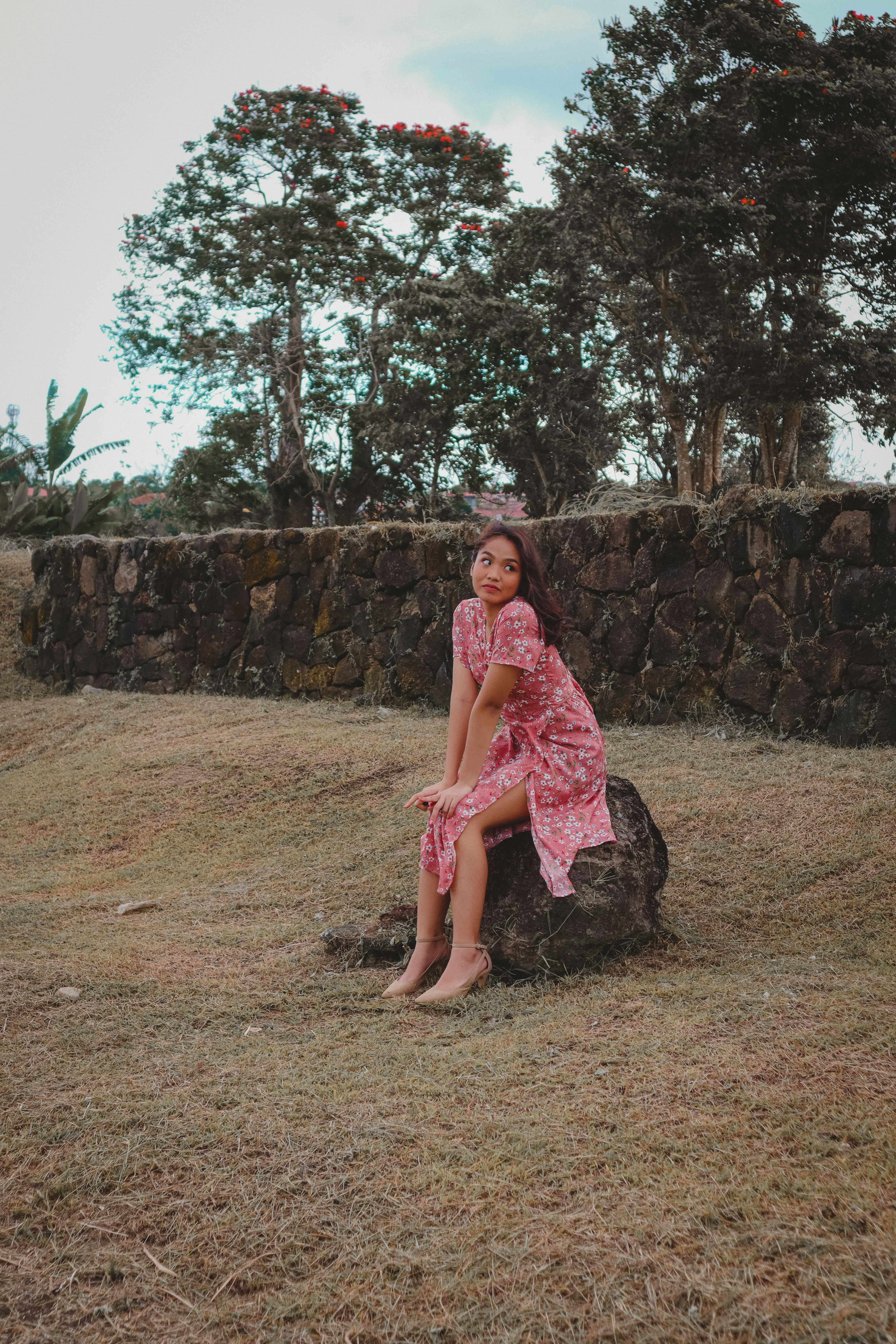 a woman in a pink dress sitting on a rock