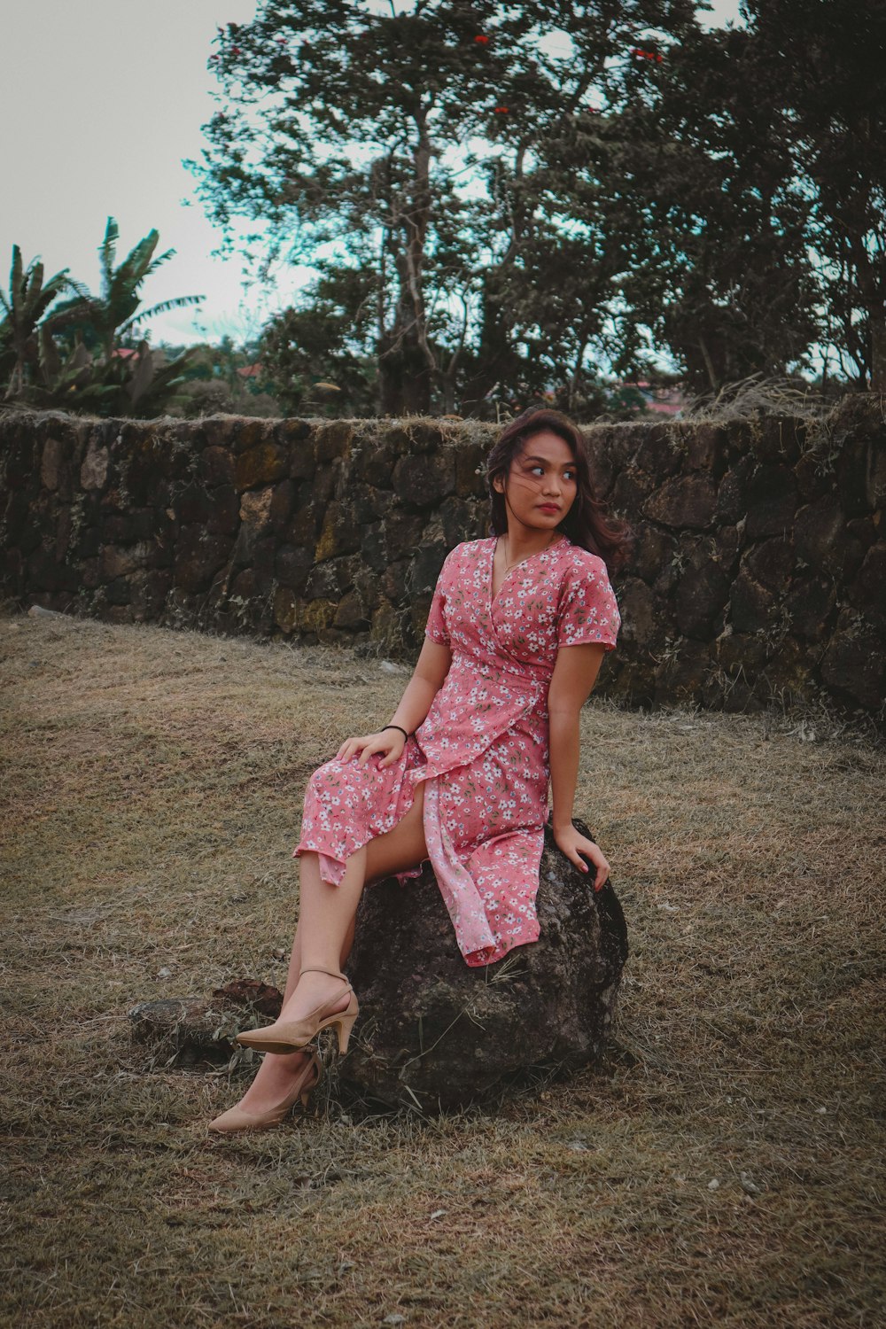 a woman in a pink dress sitting on a rock