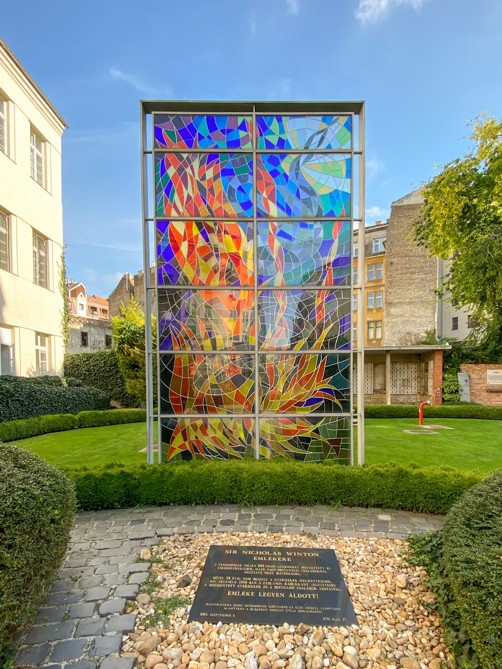a colorful stained glass window in the middle of a garden