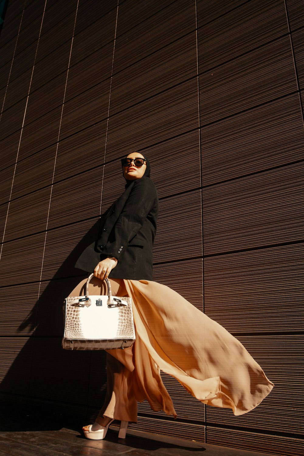 a woman in a black jacket and dress carrying a white purse